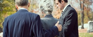 Woman being comforted by adult sons at a funeral
