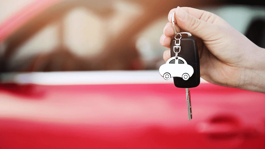 Car keys being held in front of red car