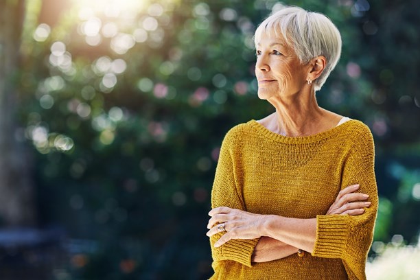 Relaxed woman with arms crossed standing in a garden