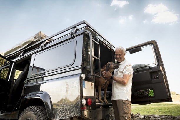 Man standing at the back of open 4x4 with dog inside