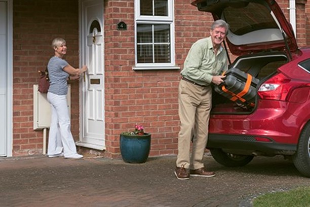 Woman locking front door while husband loads case into car boot on drive