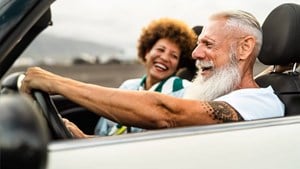 A older man and woman laughing and driving open top car