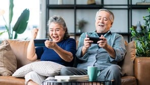 A older man and woman playing a video console on a couch