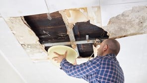 A man fixes a leak in a roof, covered by home insurance.