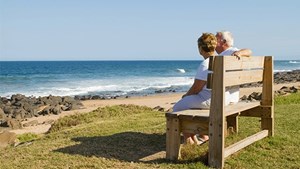 Couple sitting on a bench looking out over a beach to sea